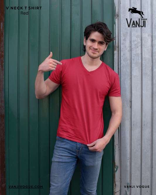 Man wearing red v neck t shirt men styled casually with blue jeans standing against green and gray wall